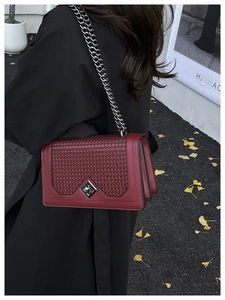 Detail of burgundy leather shoulder bag with woven flap and silver chain in autumn setting
