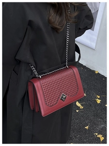 Detail of burgundy leather shoulder bag with woven flap and silver chain on a black coat