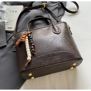 Detail of dark brown bucket bag with FASHION&BAGS embossing and beaded pendant