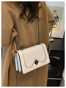 Detail of white crossbody bag with woven texture, metal chain, and accordion side design