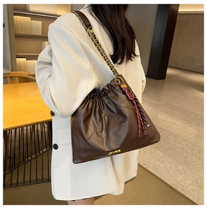 Detail of brown quilted faux leather tote bag with gold chain strap and metal logo