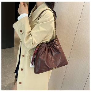 Detail of burgundy quilted leather tote bag with gold chain strap on a trench coat