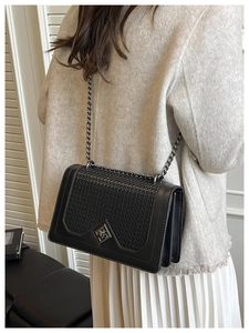 Detail shot of black woven flap bag with metal chain strap worn on the shoulder
