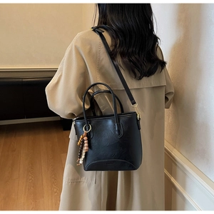 Detail of black leather bucket bag with beaded charm and gold hardware on trench coat
