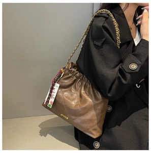 Detail of a brown quilted tote bag featuring a drawstring closure and gold chain strap