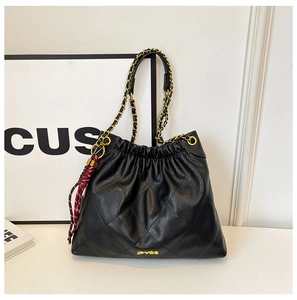 Detailed view of black quilted bucket bag with gold chain strap and decorative tassel charm