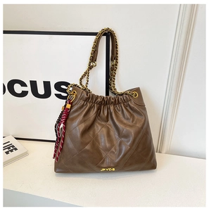 Detail of brown quilted leather tote bag featuring gold chain strap and tassel charm