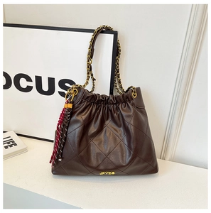 Detail of dark brown quilted leather bag with gold chain strap and colorful tassel charm
