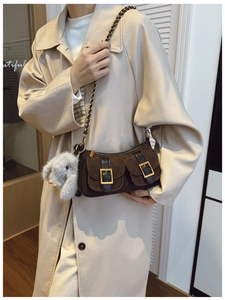 Detail of dark brown suede baguette bag with metal buckles and a plush bunny charm