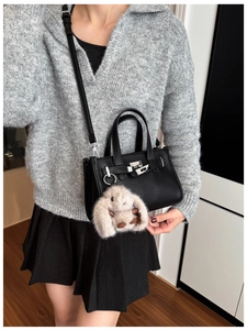 Detail of black pebbled leather handbag with silver twist lock and plush bunny charm
