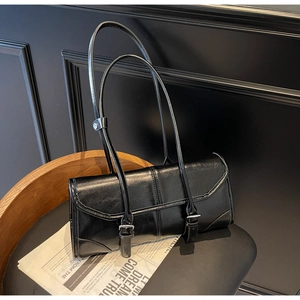 Detail of glossy black oil wax leather baguette bag on a vintage wooden chair