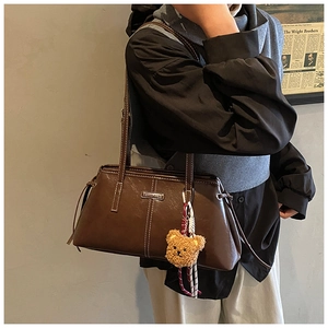 Brown leather bag with white stitching detail, metal logo plate and plush bear charm