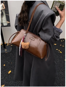 Retro brown leather shoulder bag with plush bear charm on yellow autumn leaves background