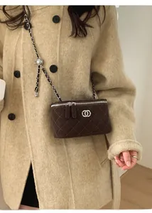 Detail of brown quilted mini box bag with silver chain strap and metal logo on coat