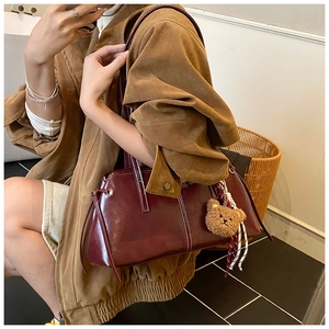Detail of dark red glossy leather shoulder bag with white stitching and bear charm