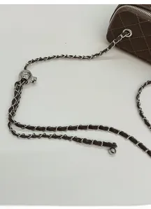 Detail of dark brown quilted crossbody bag featuring silver chain strap and ball adjuster