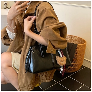 Detail of black shoulder bag with white stitching and a brown plush bear charm