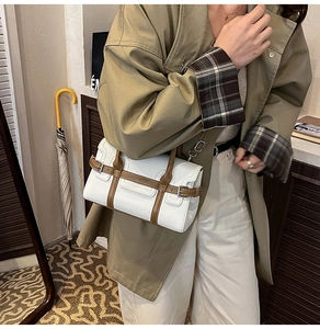 Close-up of white lychee pattern leather handbag with brown handles on beige trench coat