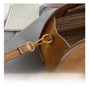 Detail des goldenen Metallhakens und des gestreiften Innenfutters der braunen Wildledertasche