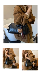 Detail of black leather shoulder bag featuring white stitching and a plush bear charm
