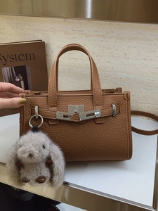 Brown litchi leather handbag with silver lock and plush bunny charm on white surface