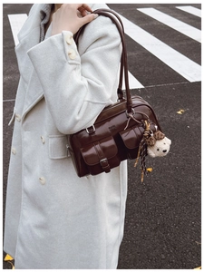 Détail d'un sac à bandoulière en cuir verni marron avec deux poches et une peluche d'ours