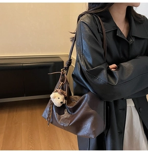 Macro detail of glossy dark brown leather shoulder bag with cute white teddy bear charm