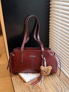Deep red vintage tote bag with white stitching and plush bear charm on a book