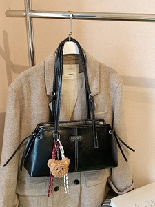 Retro black leather handbag with white stitching and plush bear charm on white hanger