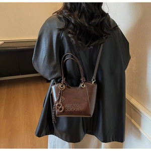 Detail of dark brown tote bag with logo embossing and tassel, styled on black leather jacket