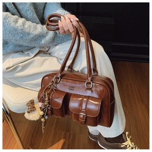 Détail d'un sac bandoulière en cuir brillant marron avec deux poches à boucle et un ours