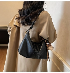 Detail of matte black leather hobo bag featuring knotted strap and cute bear charm pendant