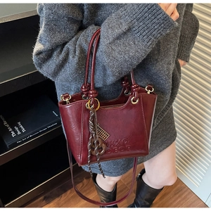 Detail of burgundy leather tote bag with embossed letters and tassel charm decoration