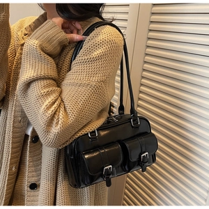 Close-up of a retro black shiny leather shoulder bag with dual silver buckle front pockets
