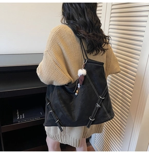 Detail of black tote bag with white contrast stitching and plush charm on a shoulder
