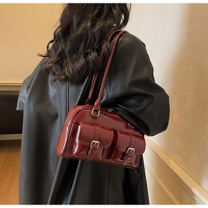 Detail view of a vintage burgundy leather shoulder bag with buckle pockets on a model