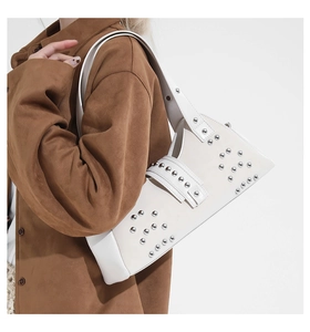 Detail view of white leather shoulder bag with silver studs on wide strap and side profile