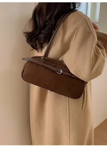 Close-up of vintage brown suede baguette bag with silver buckle and thin straps on camel coat