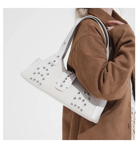 Close-up of white shoulder bag with silver studs on a model wearing a brown jacket