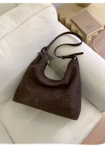 Close-up of dark brown woven leather hobo bag with star charm on a white sofa