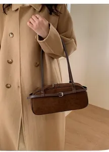 Close-up of a dark brown suede baguette bag with buckle strap on a camel wool coat
