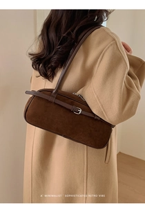 Detail of dark brown matte suede baguette bag with silver buckle worn on shoulder