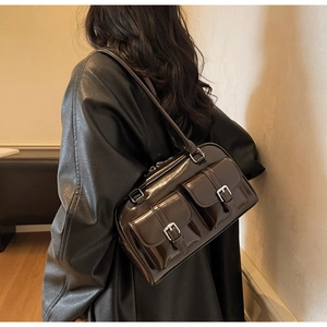Detail of dark brown glossy shoulder bag with multiple buckle pockets on a model