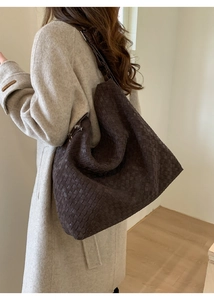 Close-up of deep brown intrecciato woven hobo bag with wide shoulder strap on beige coat