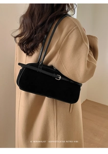 Detail of a black suede baguette bag with metal buckle worn over a camel coat