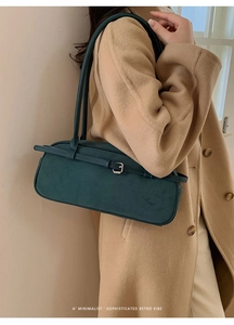 Detail of dark green suede baguette bag with decorative buckle on a camel wool coat