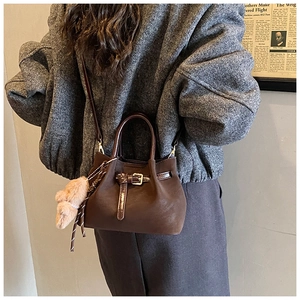Détail d'un sac seau en daim marron foncé avec lanières en cuir et breloque ours