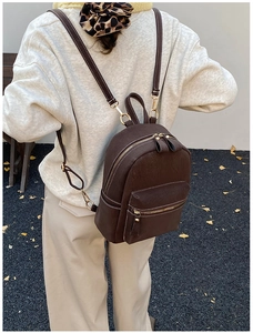 Detailed view of dark brown suede backpack with white stitching and gold hardware on model