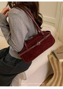 Detail of burgundy suede baguette bag with silver buckle worn as a shoulder bag