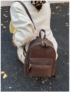 Detail of minimalist dark brown backpack with white stitching shown on autumn leaves